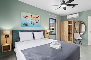 Ein modernes Hotelzimmer mit einem großen Bett, einem Deckenventilator, einem Flamingo-Gemälde, einem Kleiderschrank und einem Spiegel.