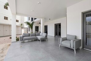 A spacious, modern outdoor living area with a grey sectional sofa and armchairs, a ceiling fan, and a large sliding glass door.