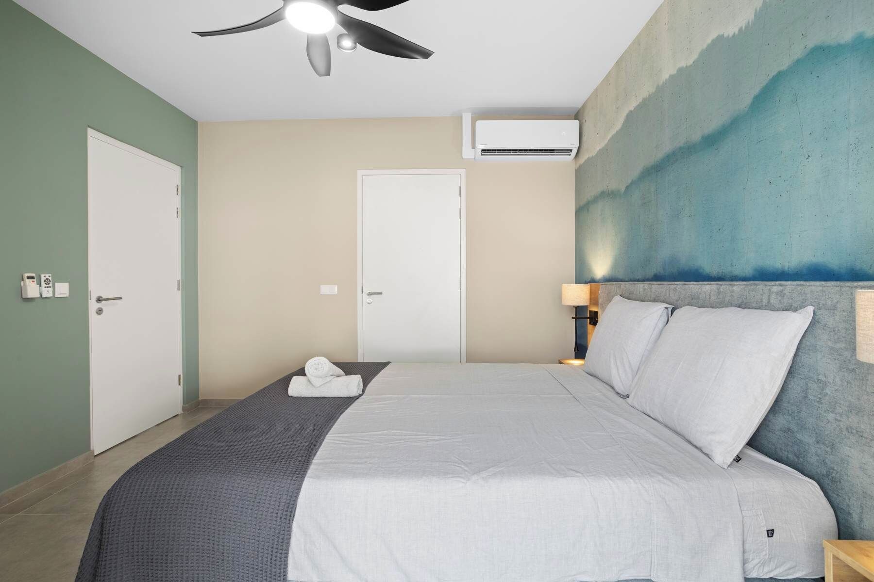 Une chambre d’hôtel équipée d’un lit, d’un ventilateur de plafond, d’un appareil de climatisation et d’un mur au décor texturé.