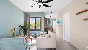 Un salón amplio con ventilador de techo, un sofá, una silla y vistas al exterior a través de un ventanal.