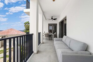 Un balcon avec un canapé gris, une table à manger avec des chaises et un ventilateur de plafond.