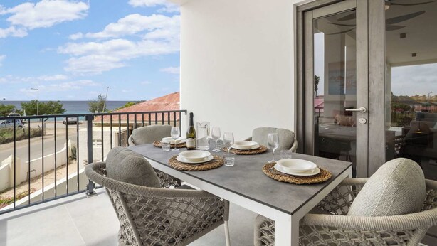 A balcony with a table set for two, overlooking a coastal area. - Bonaire Beach Apartments 6 with a refreshing shared pool and ocean view (Kralendijk)