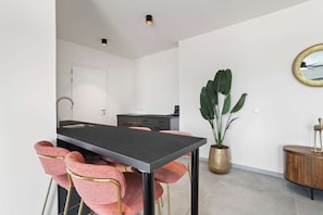A modern kitchen with a central island, a dining area with pink chairs, a large plant, and a wooden cabinet. - Bonaire Beach Apartments 6 with a refreshing shared pool and ocean view (Kralendijk)