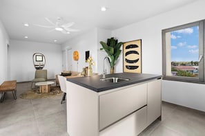 A modern kitchen with a central island, a dining area with a round table, and a view of the city through a large window.