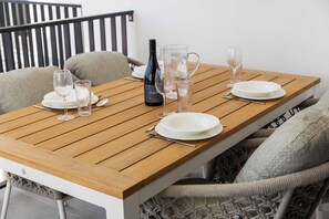 A dining table set with plates, glasses, and a bottle of wine, surrounded by cushioned chairs.