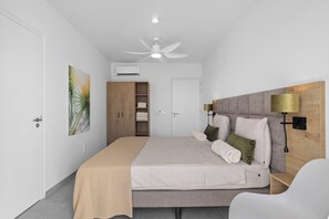 Um quarto com cama, ventoinha no teto, mesa de cabeceira, luminária e guarda-roupa.