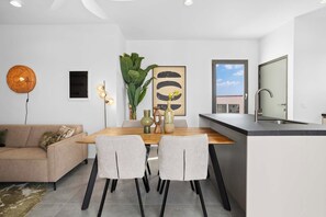 Une cuisine moderne avec un coin repas, comprenant une table en bois, deux chaises, un vase avec des fleurs et une grande fenêtre donnant sur l’extérieur.