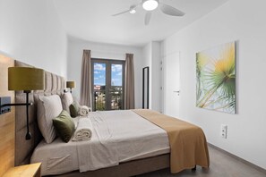 Une chambre moderne avec un lit, un ventilateur de plafond et une grande fenêtre avec des rideaux.