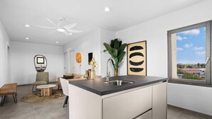 Een moderne keuken met een centraal eiland, een eethoek met een ronde tafel, en uitzicht op de stad door een groot raam.