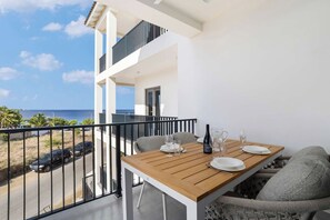 A balcony with a wooden table set for dining, overlooking a beach and ocean.