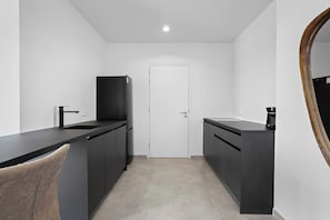 A compact kitchen with dark cabinetry, a sink, and a coffee machine.