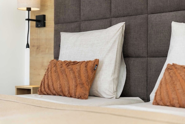 A bed with two pillows, one brown and one white, against a grey headboard.