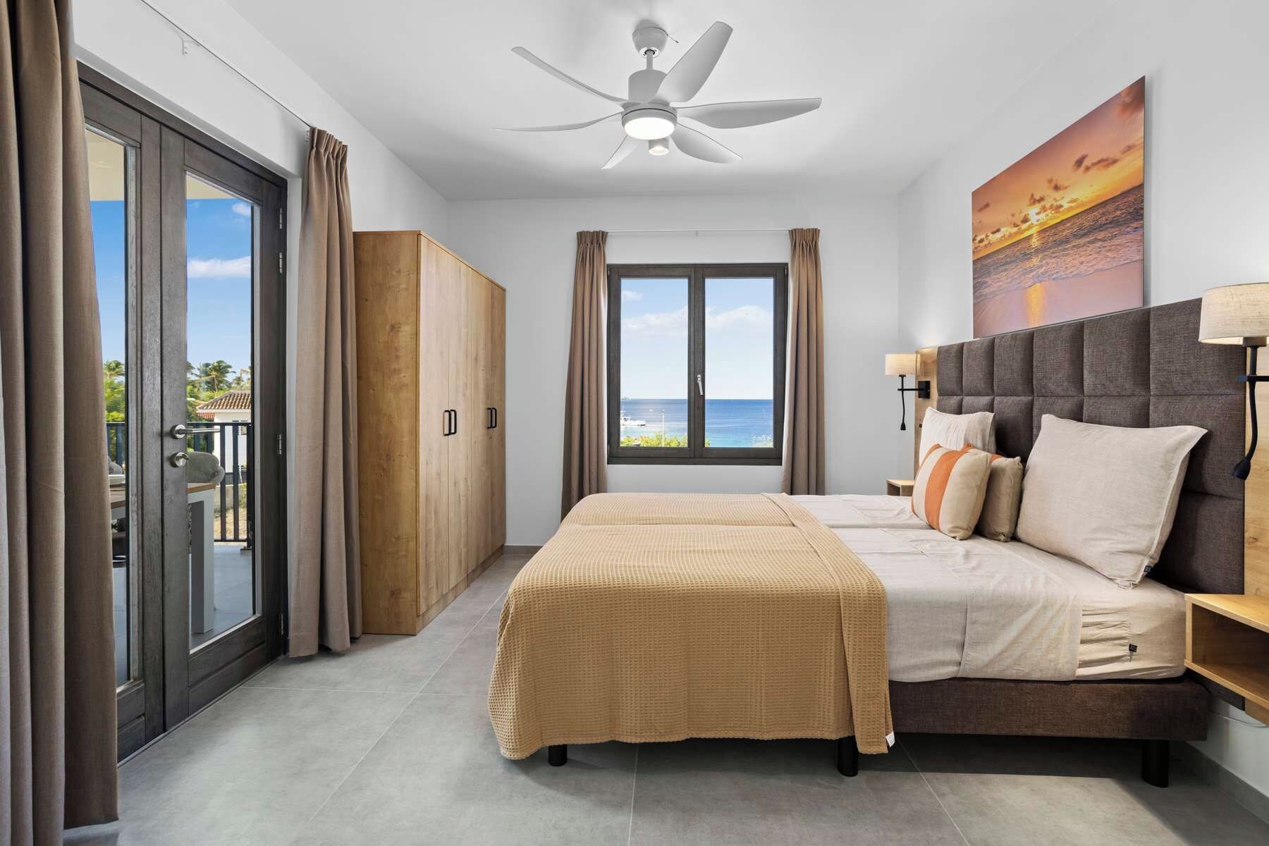 A bedroom with a bed, a ceiling fan, a view of the ocean, and a sliding door to the outside.