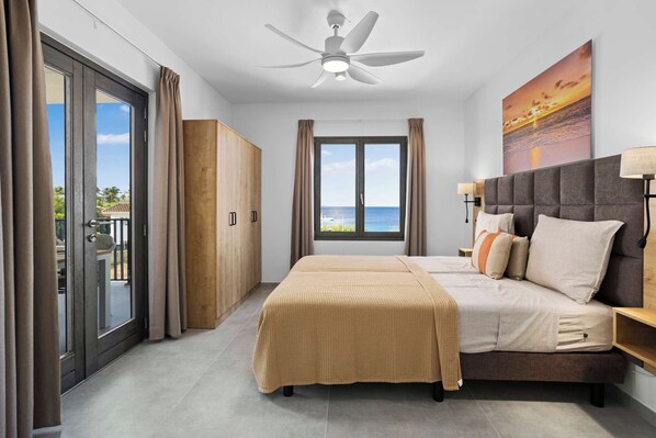 A bedroom with a bed, a ceiling fan, a view of the ocean, and a sliding door to the outside.