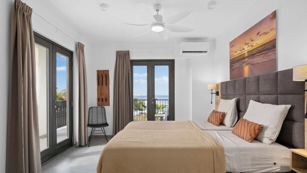 A modern hotel room with a large bed, a balcony with a view, and a ceiling fan. - Bonaire Beach Apartments 10 with a refreshing shared pool and spectacular sea views (Kralendijk)