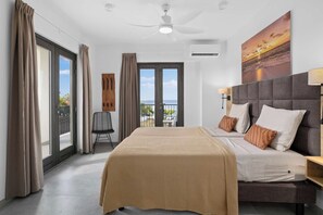 A modern hotel room with a large bed, a balcony with a view, and a ceiling fan. - Bonaire Beach Apartments 10 with a refreshing shared pool and spectacular sea views (Kralendijk)