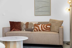 A neutral-toned sofa with four patterned cushions, a marble table, and a modern floor lamp.