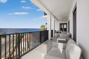 A balcony with a view of the sea, a sofa, and a table with chairs.