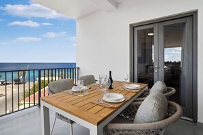 A wooden table set for dining with chairs, a view of the ocean, and a sliding glass door to the interior. - Bonaire Beach Apartments 10 with a refreshing shared pool and spectacular sea views (Kralendijk)