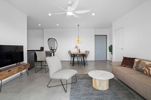 A modern living room with a flat-screen TV, a sofa, a coffee table, and a dining area with a table and chairs.