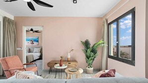 A modern living room with a grey sofa, a wooden coffee table, a small side table, a potted plant, and a view of the sky through a large window. - Bonaire Beach Apartments 12 with a mature palm garden and a lovely shared pool (Kralendijk)