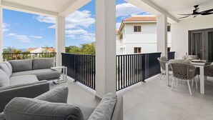 Een balkon met een bank en stoelen, een tafel met een stoel, en uitzicht op een gebouw aan de overkant van de straat.