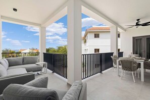 Un balcon avec un canapé et des fauteuils, une table avec une chaise, et une vue sur un immeuble situé de l’autre côté de la rue.