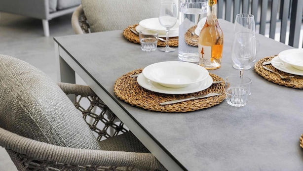 A dining table set with plates, glasses, a bottle, and a pitcher, surrounded by wicker chairs. - Bonaire Beach Apartments 12 with a mature palm garden and a lovely shared pool (Kralendijk)