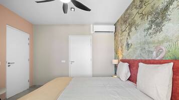 A bedroom with a bed, a ceiling fan, an air conditioning unit, a door, and a wall with a painting.