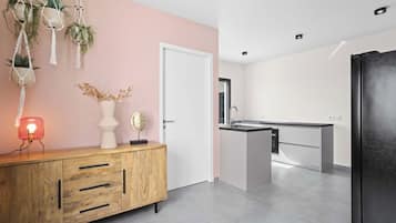 A modern kitchen with a wooden cabinet, a pink wall, and hanging plants.