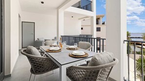 A balcony with a dining table set for four, surrounded by wicker chairs. - Bonaire Beach Apartments 12 with a mature palm garden and a lovely shared pool (Kralendijk)