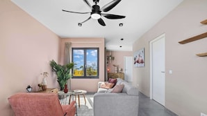 A modern living room with a grey sofa, a pink armchair, and a ceiling fan. - Bonaire Beach Apartments 12 with a mature palm garden and a lovely shared pool (Kralendijk)