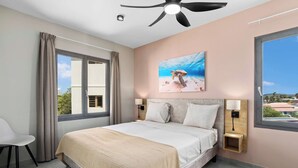 Een slaapkamer met een bed, twee nachtkastjes, een plafondventilator, een groot raam en een schilderij van een zeeschildpad.