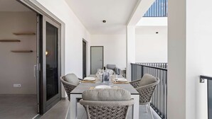 Een balkon met een eettafel voor vier personen, twee rieten stoelen en een bijzettafeltje.