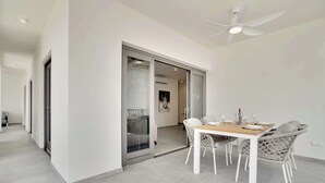 A modern dining area with a white table and chairs, a ceiling fan, and a glass door leading to a balcony. - Bonaire Beach Apartments 15 with a refreshing shared pool and spectacular sea view (Kralendijk)