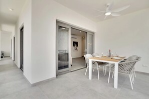 Een moderne eetruimte met een witte tafel en stoelen, een plafondventilator en een glazen deur naar een balkon.