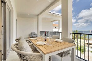 A dining area with a wooden table set for two, a sofa, and a balcony with a view of the sea.