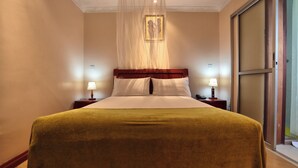 Habitación de hotel con una cama grande, dos mesitas de noche con lámparas, un ventanal con vistas y un techo con diseño decorativo.