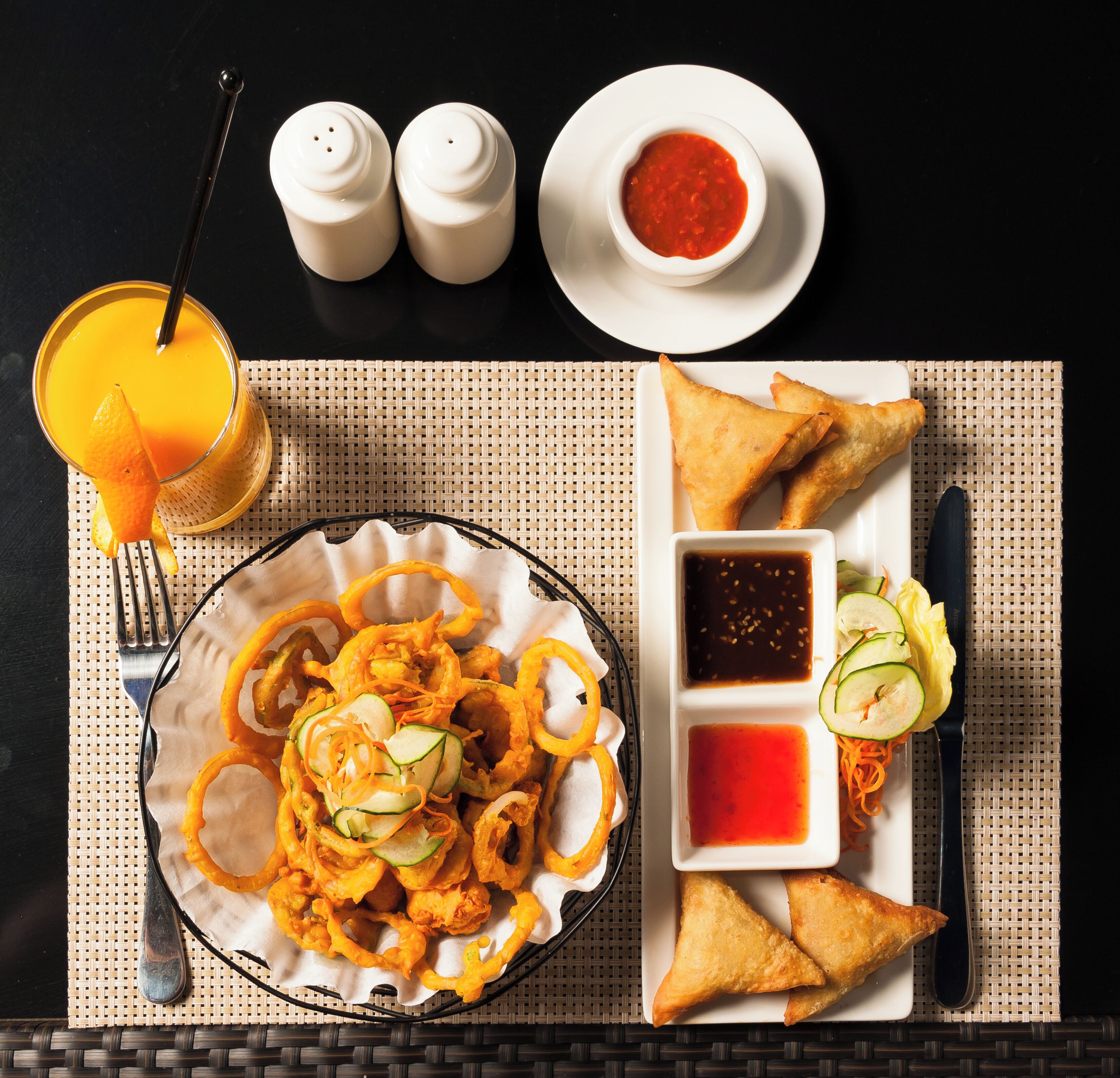 Un plato con aperitivos fritos, un vaso de zumo de naranja y salsas sobre una mesa.