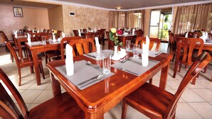 Un comedor con varias mesas y sillas de madera, cada conjunto con servilletas blancas, cubiertos y cristalería.