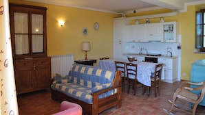 A cozy living room with a sofa, chairs, and a dining table. There is a kitchen area with cabinets and a sink. - Charming Flat With Pool Surrounded by Nature (Asciano)