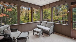 A sunroom with large windows, wicker furniture, and a ceiling fan. - Red Hemlock Retreat | Hot Tub & Close To Mountains (Wardsboro)