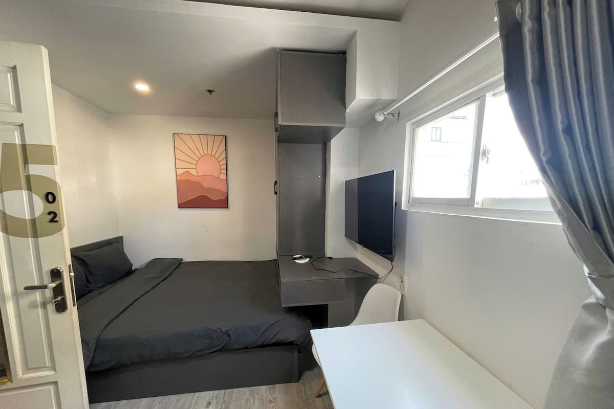 A compact hotel room with a bed, a desk, a chair, a TV, and a window with curtains.