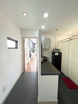 A narrow hallway with a kitchen area on the right, featuring a refrigerator, sink, and a small countertop. A window with a view of a balcony is visible on the left. - Home Away Dang Thi Nhu (Ho Chi Minh City)