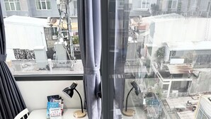 Una habitación con un gran ventanal, una mesa blanca con algunos libros y una lámpara, y vistas a la ciudad.