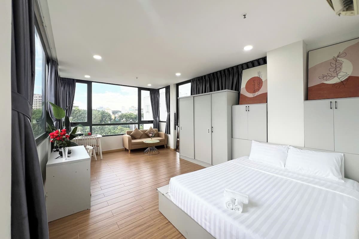 A modern bedroom with a large bed, a sofa, a desk, and a view of the city.