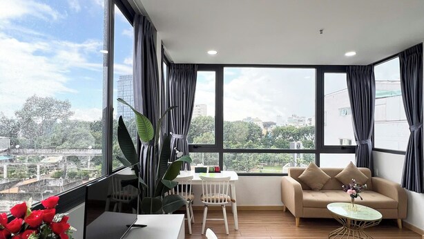 Un salón moderno con un sofá, una mesa de centro y un escritorio con una computadora. Amplias ventanas ofrecen vistas de la ciudad.