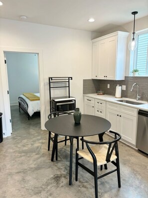 A modern kitchen with white cabinets, a stainless steel sink, and a round table with chairs. - NEW-Teche House-KING Bed-Cajun Getaway-Fast Wi-Fi (Lafayette)