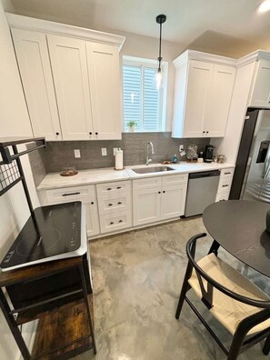 A modern kitchen with white cabinets, a built-in oven, a sink, and a dining area with a table and chairs. - NEW-Teche House-KING Bed-Cajun Getaway-Fast Wi-Fi (Lafayette)