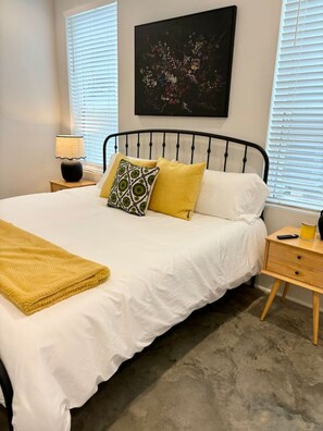A bedroom with a bed, a nightstand, a lamp, and a painting on the wall. - NEW-Teche House-KING Bed-Cajun Getaway-Fast Wi-Fi (Lafayette)